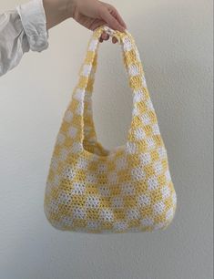 a hand holding a yellow and white crocheted bag on a hook against a wall