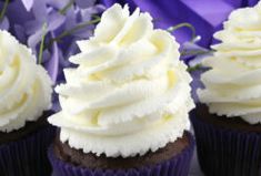 three cupcakes with white frosting and purple flowers