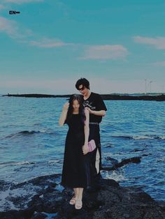 a man standing next to a woman on top of a rocky beach near the ocean