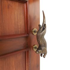 a wooden door with a metal animal handle on it's left side and a white wall in the background