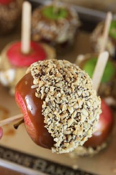 someone holding an apple covered in chocolate and sprinkled with nuts on a stick