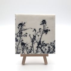 a white and black tile with flowers on it sitting on top of a wooden stand