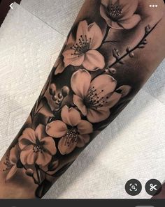 a black and white tattoo with flowers on the arm, in front of a phone