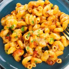 a blue plate topped with pasta covered in sauce and cheese next to a silver fork