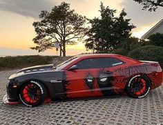 a red and black car parked on top of a brick road next to a house