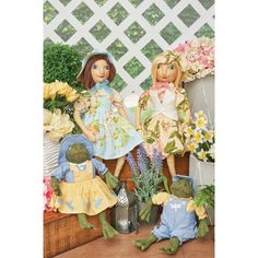 two dolls sitting next to each other in front of flowers and potted planters