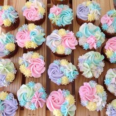 cupcakes with different colored frosting are arranged on a wooden table in rows