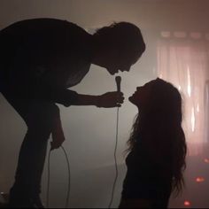 a woman holding a microphone next to a silhouette of a man with long hair on stage