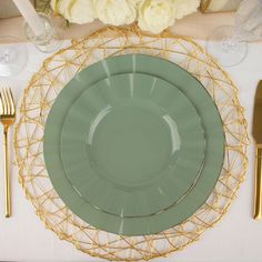 there is a place setting on the table with gold cutlery and flowers in the background