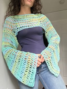 a woman wearing a crocheted sweater and jeans standing next to a white wall