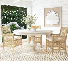 a white table with chairs around it in front of an open window and flowers on the wall