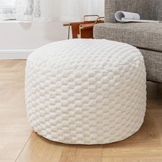 a white round ottoman sitting on top of a hard wood floor next to a gray couch