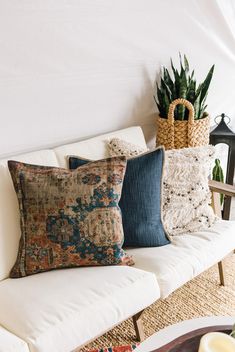 pillows on a white couch in front of a potted plant and wicker basket