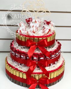 a three tiered cake with red ribbon and white chocolates on it's sides