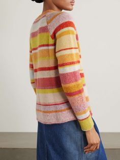 a woman wearing a multicolored striped sweater and denim skirt, looking off to the side