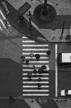 black and white photograph of an overhead view of people crossing the street with umbrellas