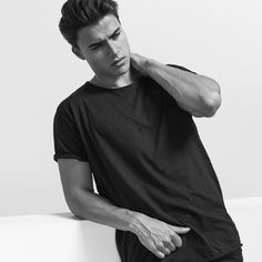 a young man sitting on top of a white bench wearing a black shirt and shorts