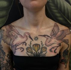 a woman with tattoos on her chest is looking at the camera and has two birds flying over her shoulder