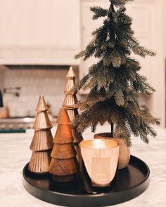 a small christmas tree sitting on top of a black tray next to a lit candle