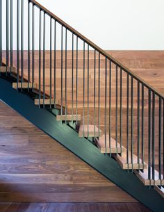 a wooden stair case with metal handrails in a wood floored area next to a wall