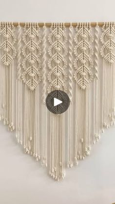 a white wall hanging with some tassels and a video play button on it