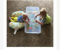 two toddlers playing with toys on the floor in front of a plastic container filled with water