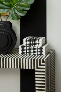 a black and white table topped with plates next to a potted plant on top of a wooden shelf