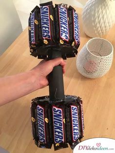 a person is holding some chocolate bars in their hand on a wooden table next to a white vase