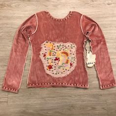 a pink top with an embroidered bear on the front and back, sitting on a wooden floor