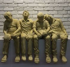 four statues of three men sitting next to each other in front of a brick wall