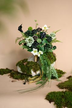 a vase filled with flowers and greenery sitting on top of a moss covered ground