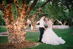 a bride and groom standing in front of a tree with fairy lights on the branches