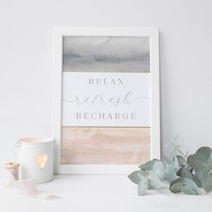 a coffee cup and some plants on a white table next to a framed poster with the words relax refresh recharge