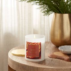 a white candle sitting on top of a wooden table next to a potted plant