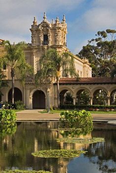 an old building with water in the foreground and lily pads on the pond below