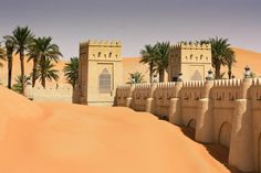 a desert with sand dunes, palm trees and two towers in the background on a sunny day