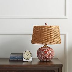 a table with a lamp, clock and books on it next to a white wall