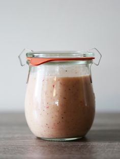 a glass jar filled with food sitting on top of a wooden table next to a red spoon