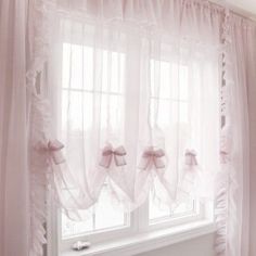 a window with sheer curtains and pink bows on the valance in front of it