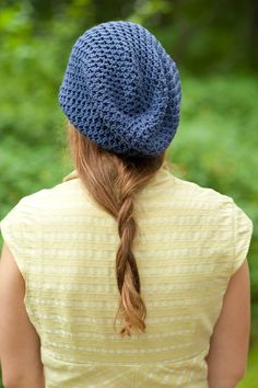 a woman with long hair wearing a blue knitted hat in front of some trees