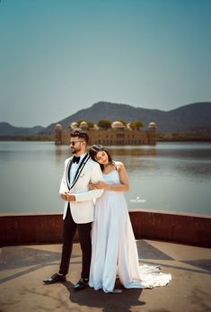 a man and woman standing next to each other in front of a body of water