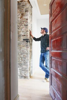 a man standing next to a red door in a room with white walls and wood floors