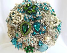 a bridal bouquet with green, white and blue jeweled brooches on it