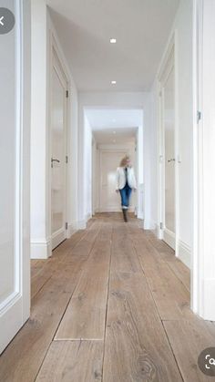 a woman walking down a long hallway with white walls and wood flooring on both sides