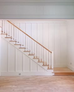 an empty room with stairs and hard wood flooring on the side, in front of a white painted wall