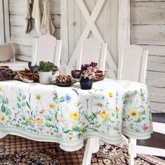 a table with flowers and plates on it in front of a white wall, next to a rug