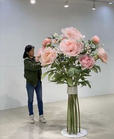 a woman standing next to a vase with flowers in it