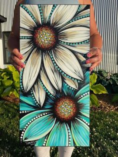 a woman holding up a painting in front of her face with flowers painted on it