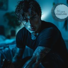 a man with tattoos sitting on a bed looking at his cell phone in the dark