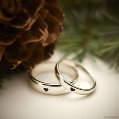 two wedding rings with hearts on them sitting next to a pine cone and pine cones